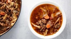 bowl of keto beef and cabbage soup on table next to pot of soup