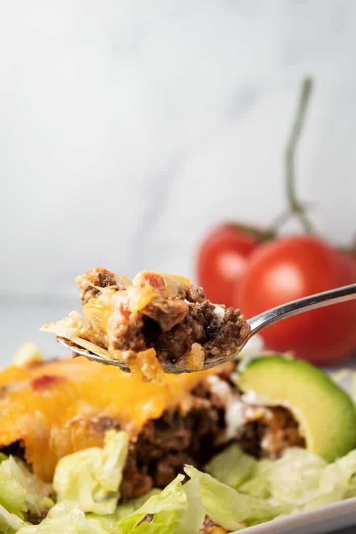 spoon full of beef held up in front of keto taco casserole with lettuce and avocado