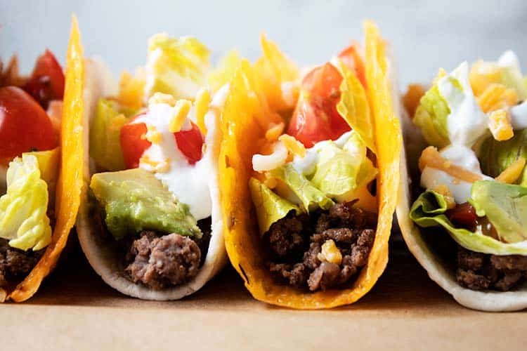 2 cheese shell keto tacos and 2 tortilla keto tacos lined up together filled with meat, lettuce, tomato, sour cream and avocado
