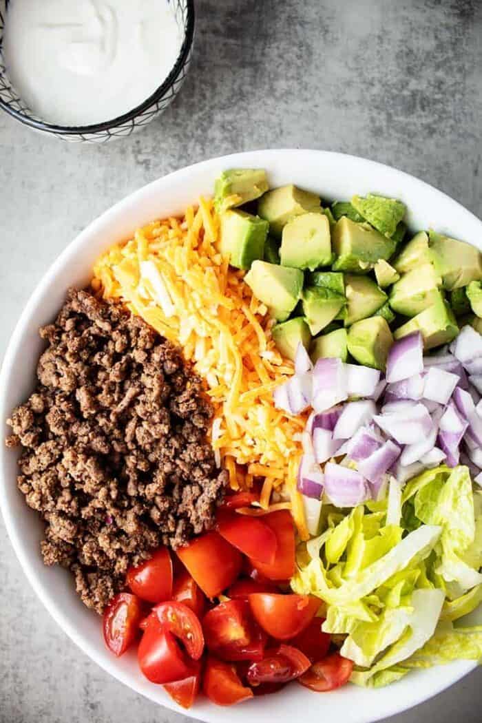 large white bowl containing keto taco salad next to a small bowl containing sour cream