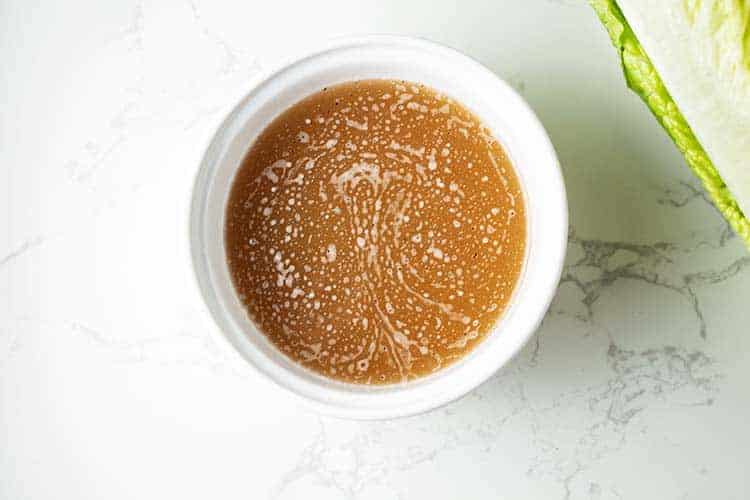 small bowl of bacon grease dressing for wilted lettuce salad next to a head of romaine lettuce