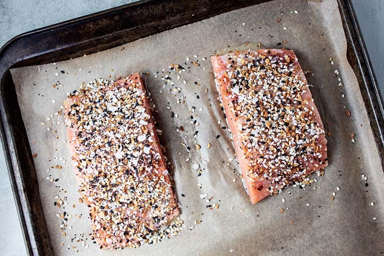 two salmon fillets covered with seasoning on a cookie sheet topped with parchment paper