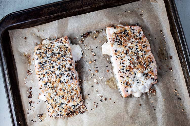 fully baked salmon fillets with everything bagel seasoning on a baking sheet with parchment paper