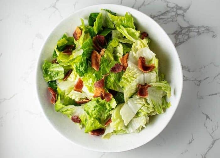 closeup of white bowl containing wilted lettuce salad with bacon