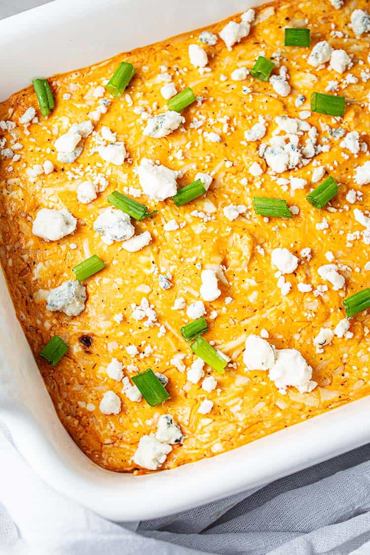 overhead view of white cassserole dish with orange colored keto buffalo chicken dip with blue cheese and chopped green onion sprinkled on top