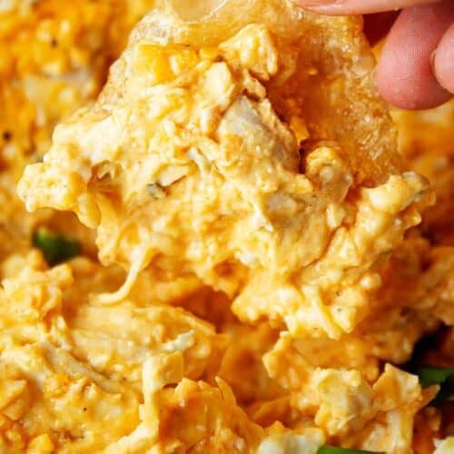 closeup view of persons hand holding a tan pork rind and dipping it into orange colored keto buffalo chicken dip