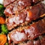 overhead view of sliced keto meatloaf with ketchup glaze on a white serving dish and carrots and broccoli on the side