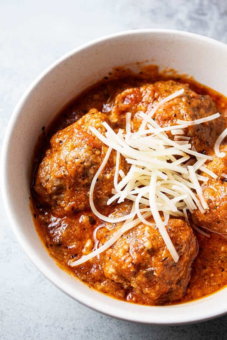 overhead view of keto meatlballs in marinara sauce topped with shredded parmesan cheese in a white serving bowl