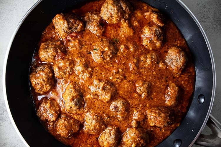 overhead view of cooked keto meatballs with marinara sauce added cooking on stovetop in a black skillet