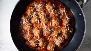 overhead view of keto meatlballs in marinara sauce topped with shredded parmesan cheese in a black skillet
