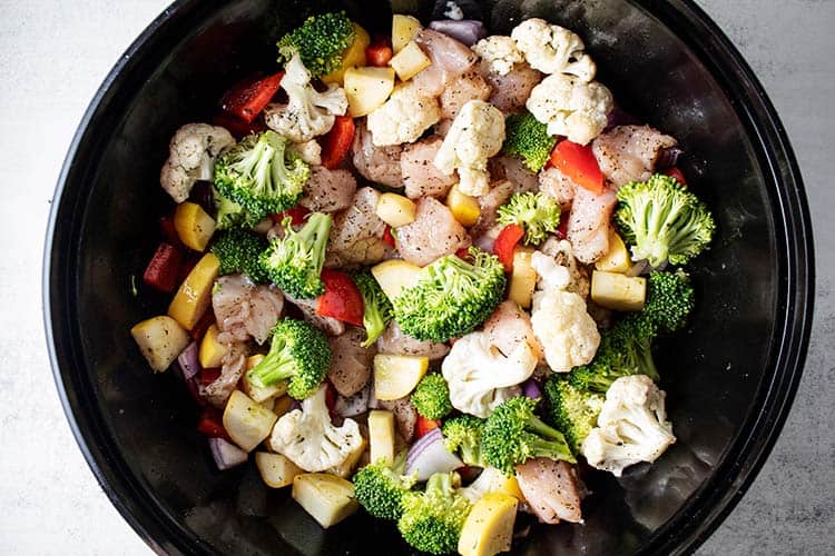 overhead view of raw chopped chicken and vegetables with seasoning added in a black mixing bowl
