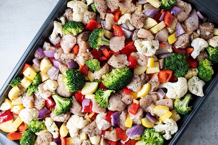 overhead view of unbaked chicken and vegetables spread evenly on a metal sheet pan