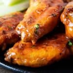 sideview of air fryer buffalo hot wings on a black serving plate with broccoli and blue cheese on the side
