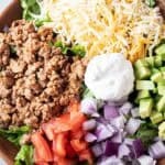 overhead view of turkey taco salad in a wooden bowl with sections of ground turkey, cheese, chopped avocado, chopped tomato, chopped onions and sour dream in the middle, all on a bed of lettuce
