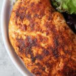 overhead view of air fryer chicken breast ready to serve on a white plate with greens and cauliflower rice on the side
