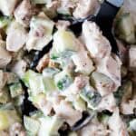 overhead view of chicken cucumber salad in a serving bowl with black serving spoon removing a serving portion