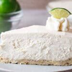 sideview of slice of keto no bake key lime cheesecake on a white serving dish topped with lime wedge and whipped cream