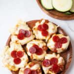overhead view of seven zucchini pizza bites on a wooden plate ready to serve
