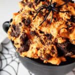 sideview of keto Halloween brownie cheesecake fluff that is dyed orange in a black cauldron on a Halloween decorated dish