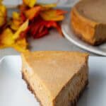 sideview of slice of keto pumpkin cheesecake on a white serving dish with the rest of the cheesecake in the background