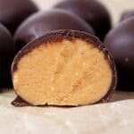 sideview of keto peanut butter balls on countertop and one of them is cut in half revealing the peanut butter interior, ready to serve
