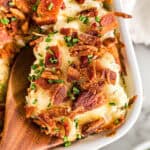 overhead view of cauliflower au gratin in a casserole dish and a portion being scooped out by a wooden spoon