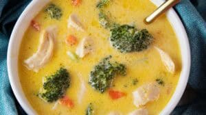overhead view of a white serving bowl of low carb keto broccoli and cheese soup with chicken and a gold soup spoon