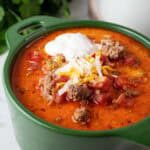 sideview of a bowl of keto taco soup topped with sour cream and Mexican shredded cheese