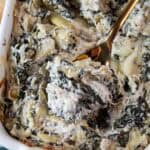 overhead view of keto spinach artichoke dip ready to serve in a white casserole dish with a gold serving spoon