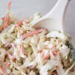 sideview of ready to serve keto coleslaw with a white serving spoon