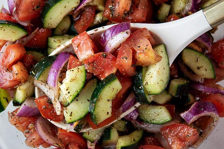 overhead view of cucumber and tomato salad ready to be served with a white serving spoon