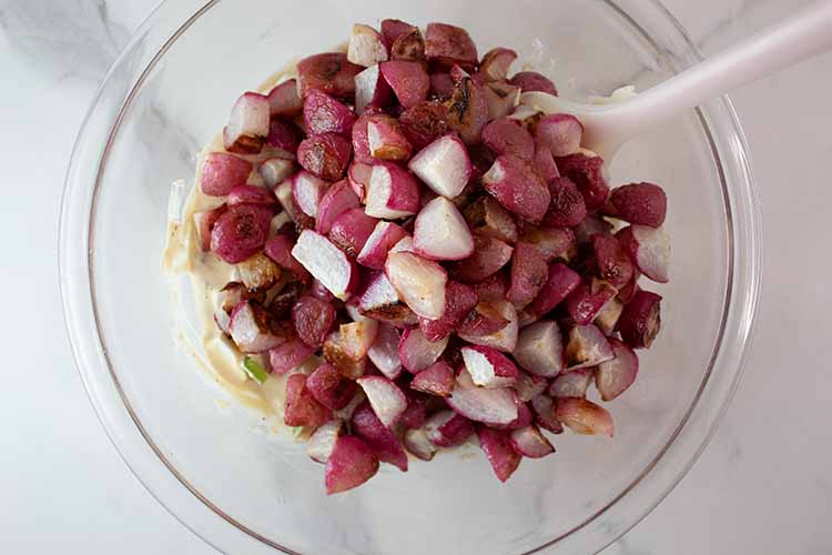 overhead view of baked radishes added to dressing ready to be lightly tossed to combine