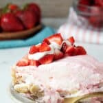sideview of a serving of keto no-bake strawberry cheesecake on a dish topped with sliced strawberries and whipped cream