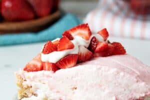 sideview of a serving of keto no-bake strawberry cheesecake on a dish topped with sliced strawberries and whipped cream