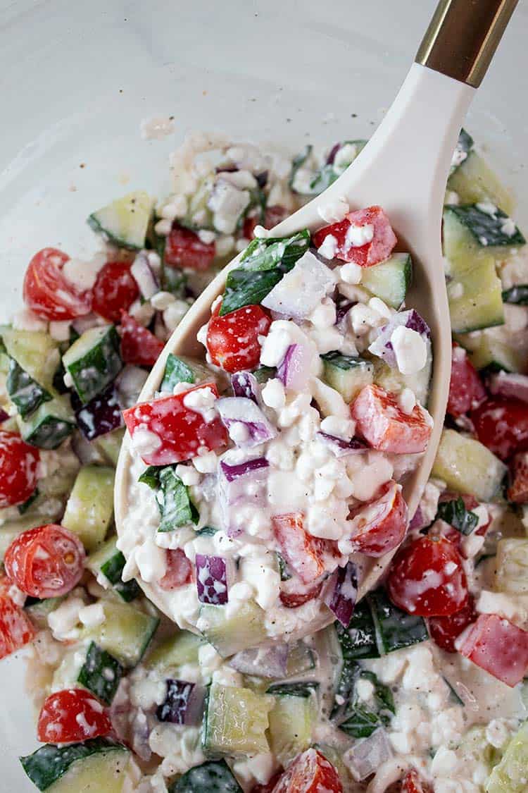 Overhead view of cottage cheese salad in a glass serving dish with a white serving spoon that removes a portion size