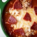 overhead view of pizza soup topped with mozzarella cheese and crispy pepperoni ready to serve in a green bowl