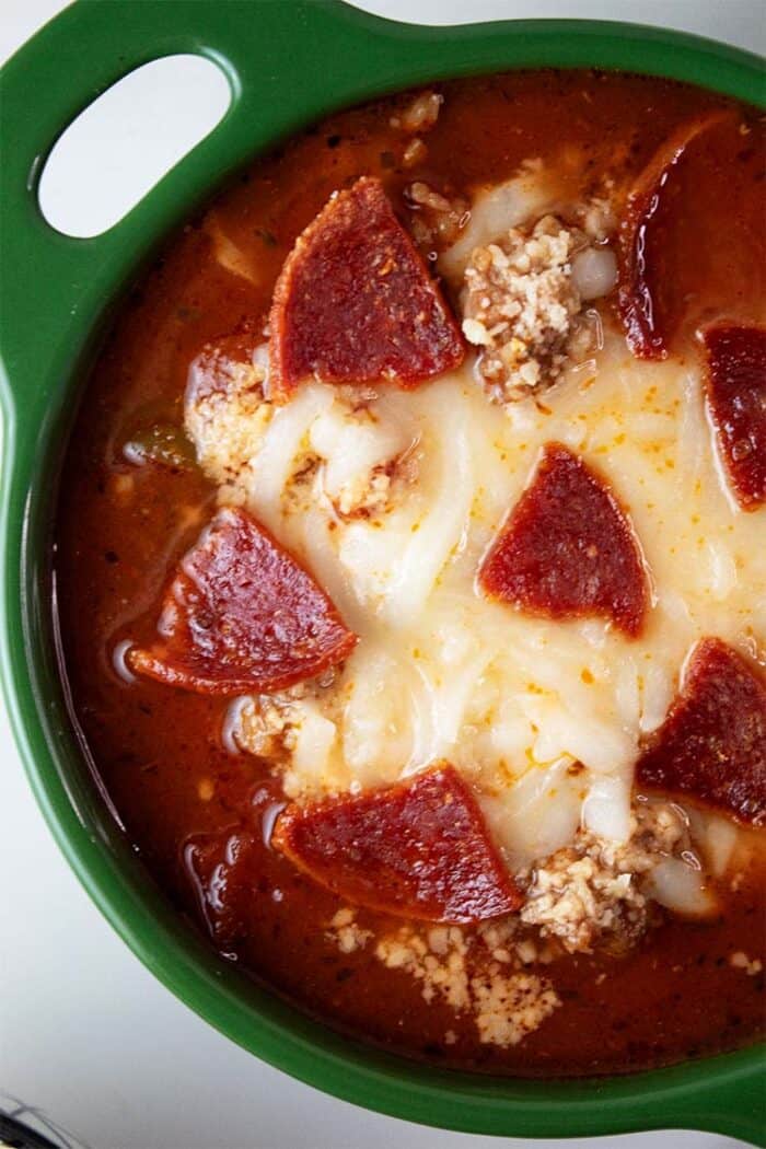 overhead view of pizza soup topped with mozzarella cheese and crispy pepperoni ready to serve in a green bowl