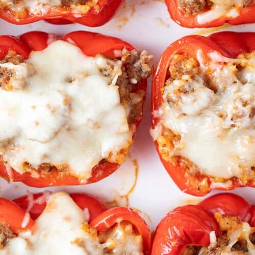 overhead view of six Italian sausage stuffed peppers evenly spaced on a serving dish