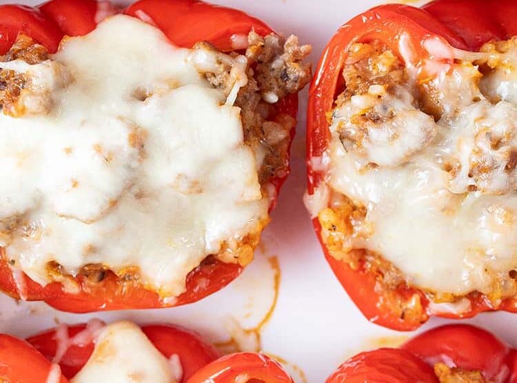 overhead view of six Italian sausage stuffed peppers evenly spaced on a serving dish