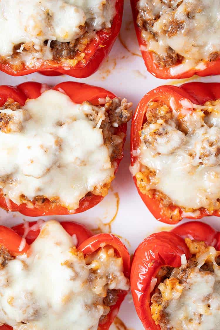 overhead view of six Italian sausage stuffed peppers evenly spaced on a serving dish