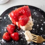overhead view of keto strawberry cheesecake on a black serving dish and gold fork topped with strawberries